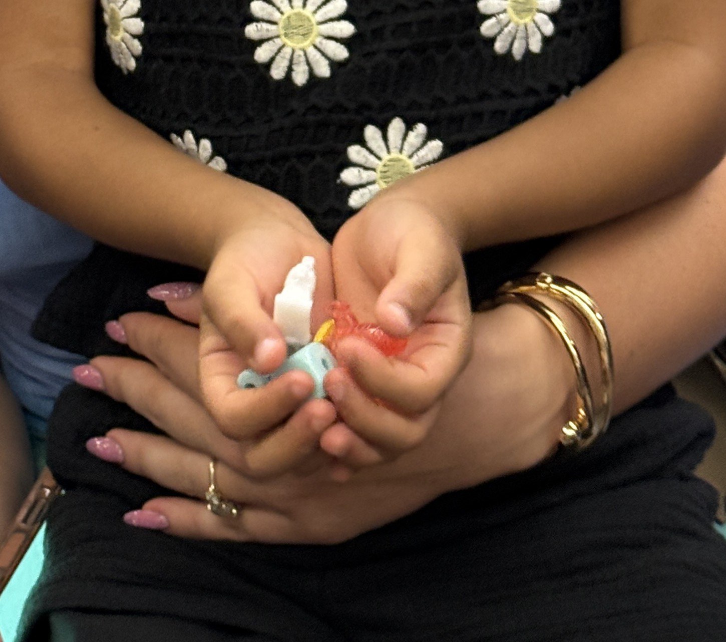Two people's hands holding pastel beads against a black floral dress