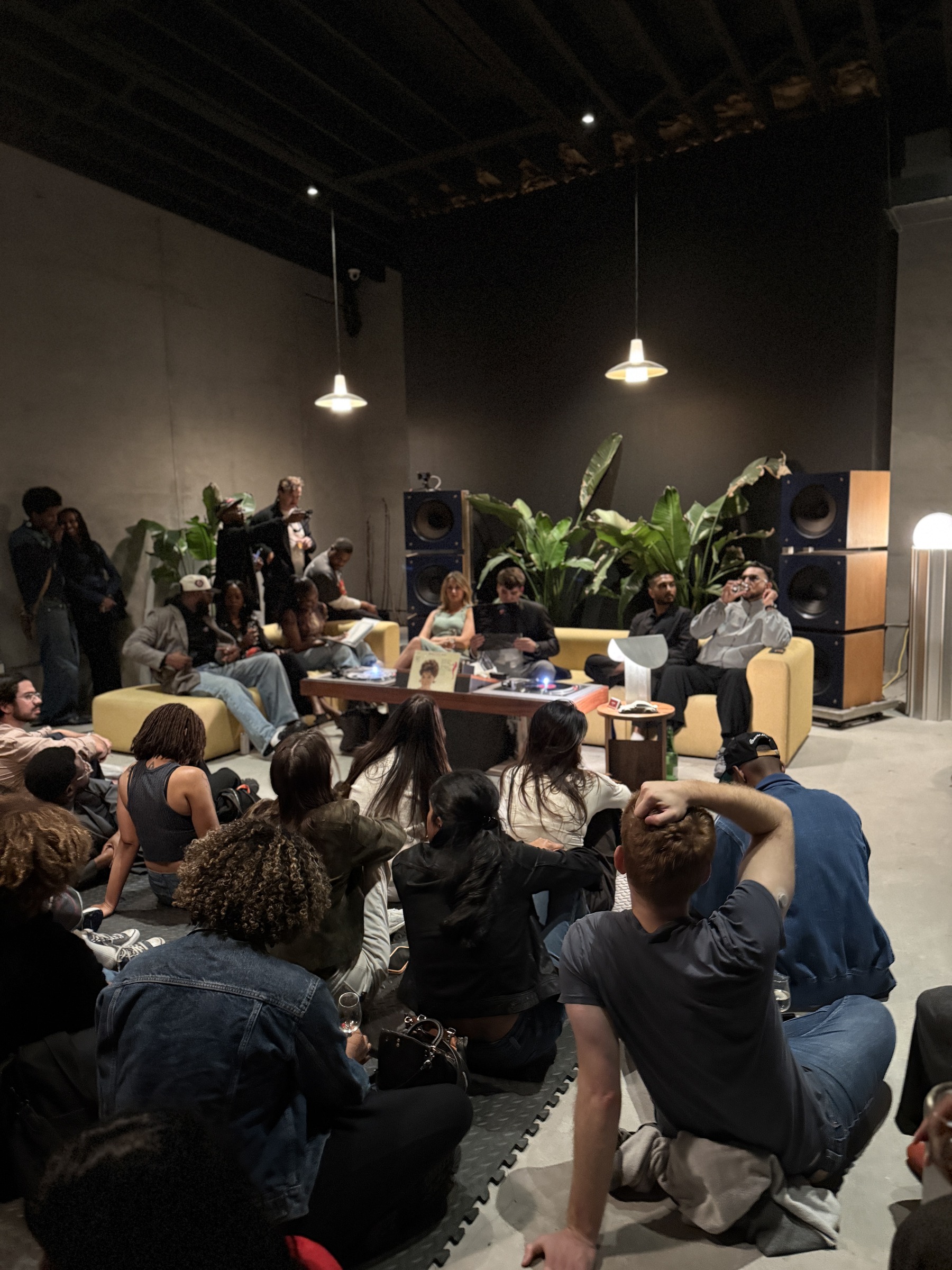 The audience seated on the floor facing the turntables