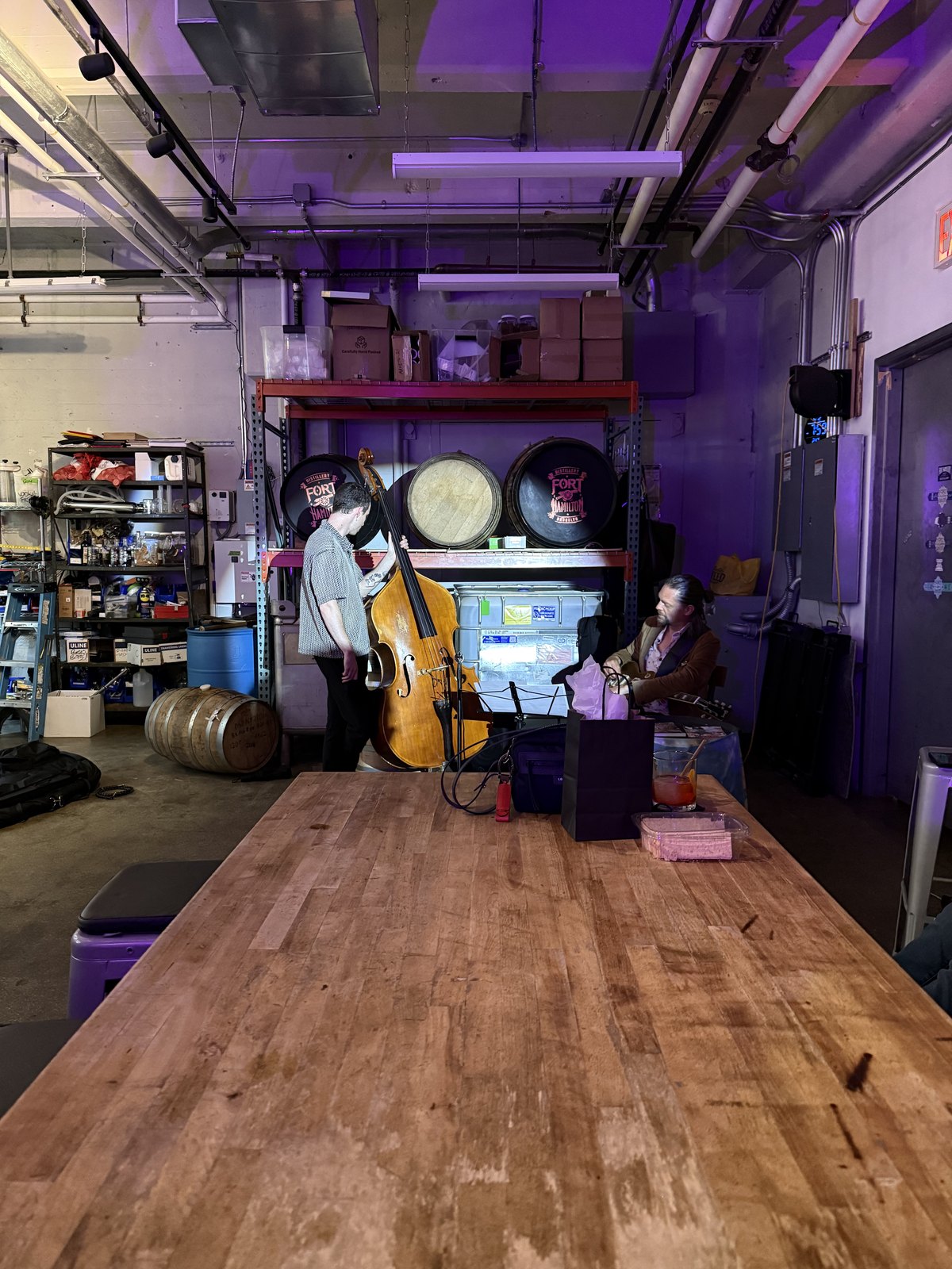 Wide view of the room — musicians at the back wall, wooden bar table in the foreground